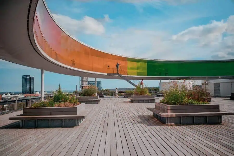 A visitor walks along the famous rainbow panorama rooftop walkway at ARoS Aarhus Art Museum, with sweeping views of the city skyline — a highlight of any Aarhus and Denmark itinerary