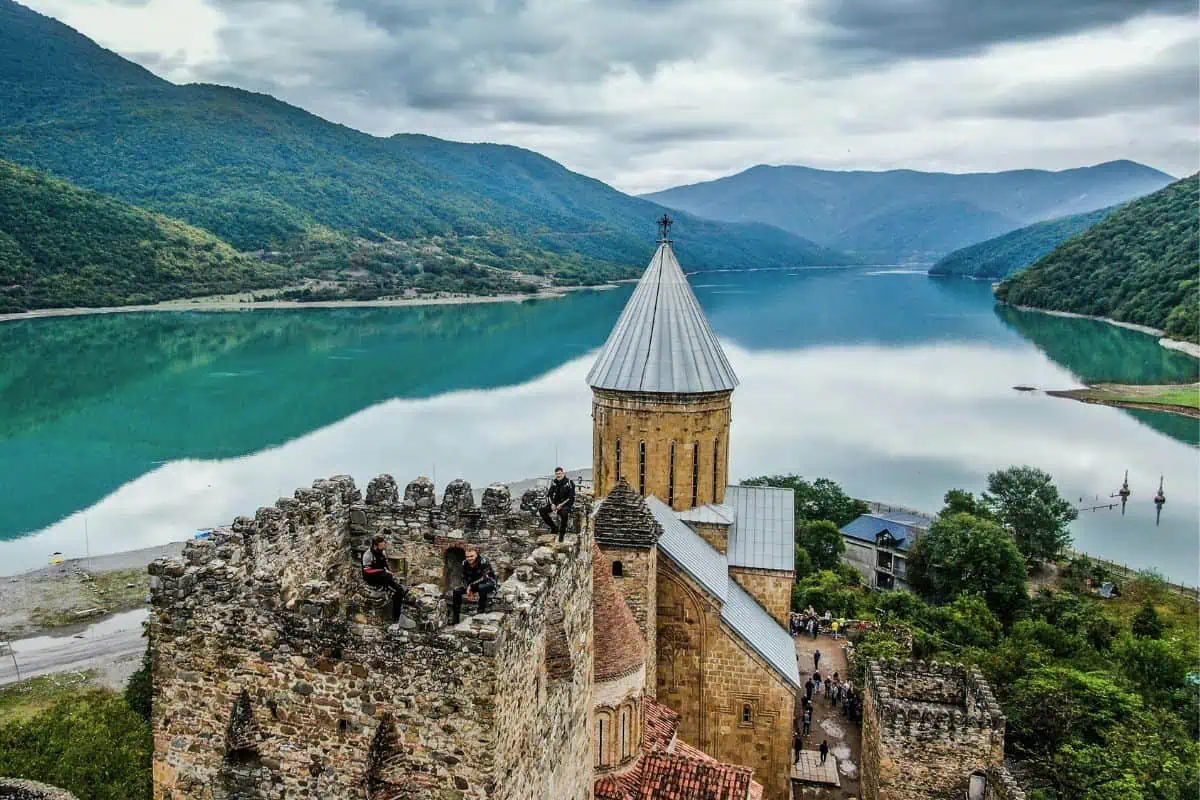 Panoramic view of Ananuri Fortress overlooking the turquoise waters of Zhinvali Reservoir, surrounded by lush green mountains under a cloudy sky in Georgia