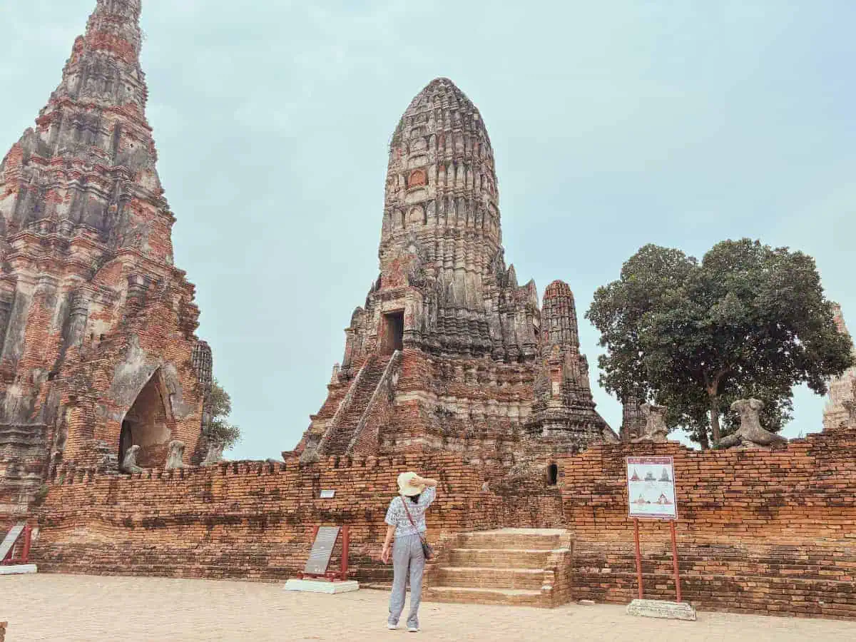 me standing near the ancient brick ruins of wat chaiwatthanaram in ayutthaya, thailand, wearing a hat and exploring the historic site