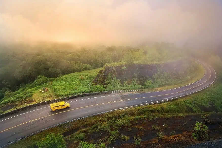 winding mountain road surrounded by lush greenery and mist, with a yellow vehicle driving through the scenic landscape