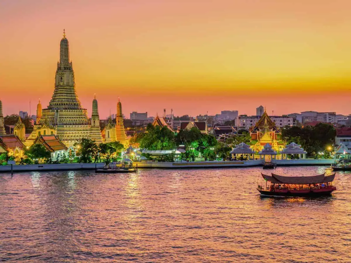 stunning sunset view of wat arun temple in bangkok, thailand, with the chao phraya river in the foreground and a traditional boat sailing past
