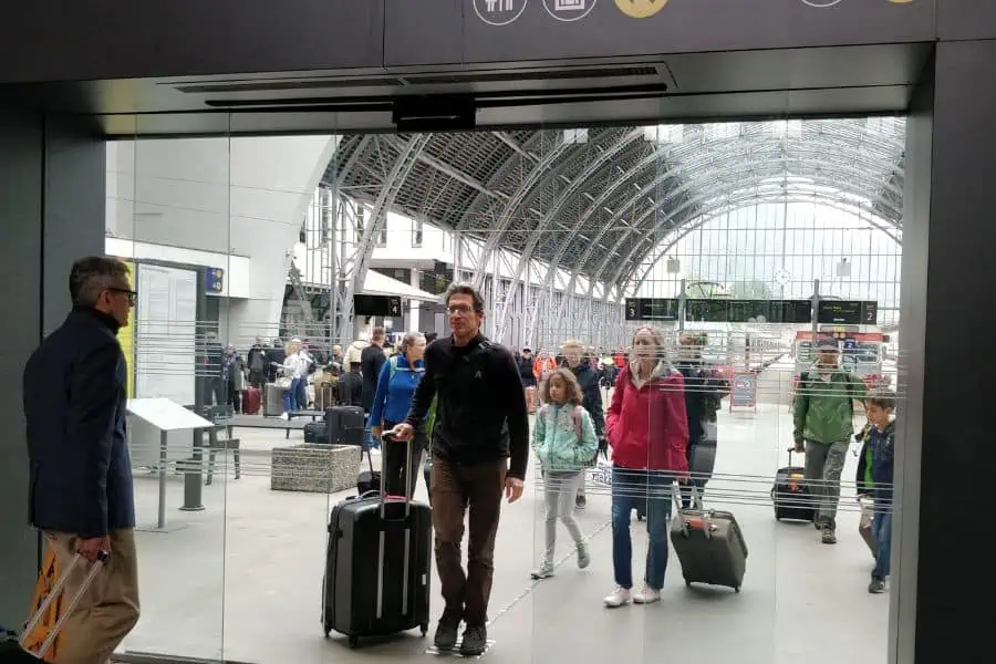 Travelers walking with luggage at Bergen train station in Norway with glass architecture and a busy concourse