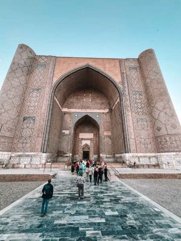 bibi khanum mosque main entrance in samarkand with towering tiled arch and visitors walking up marble steps