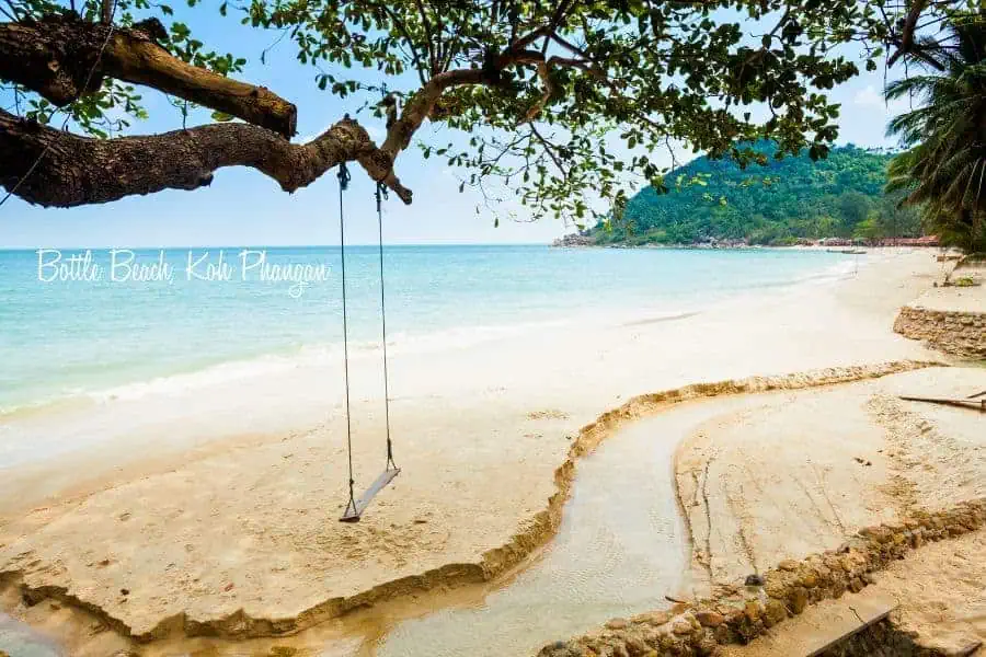 peaceful bottle beach on koh phangan, thailand, with a wooden swing hanging from a tree over soft white sand and calm turquoise water