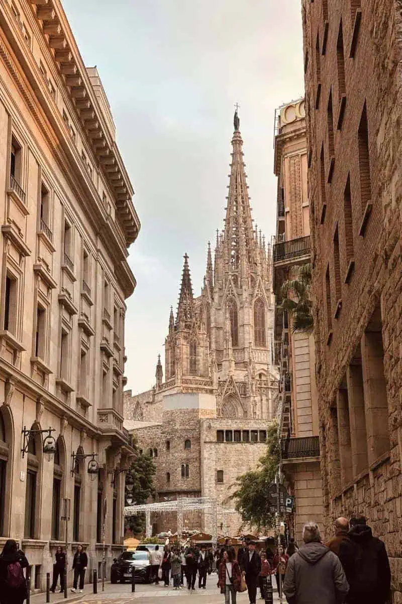 people walking on narrow street lined with historic buildings leading towards the gothic barcelona cathedral in barcelona, spain