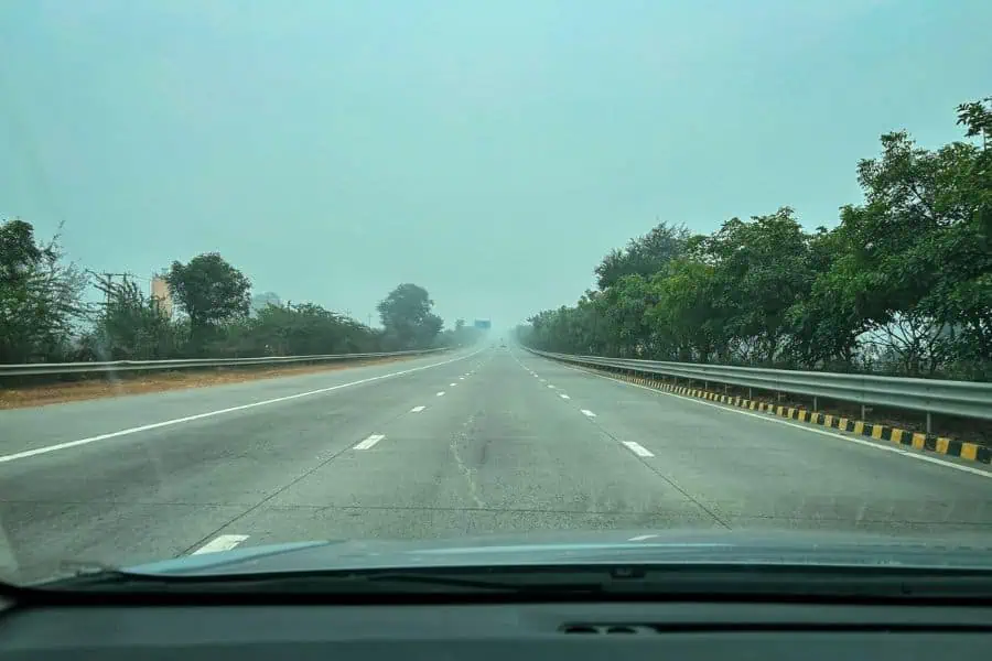 empty delhi to lucknow highway with smooth road, green trees on both sides, and a hazy morning sky, seen from inside a car