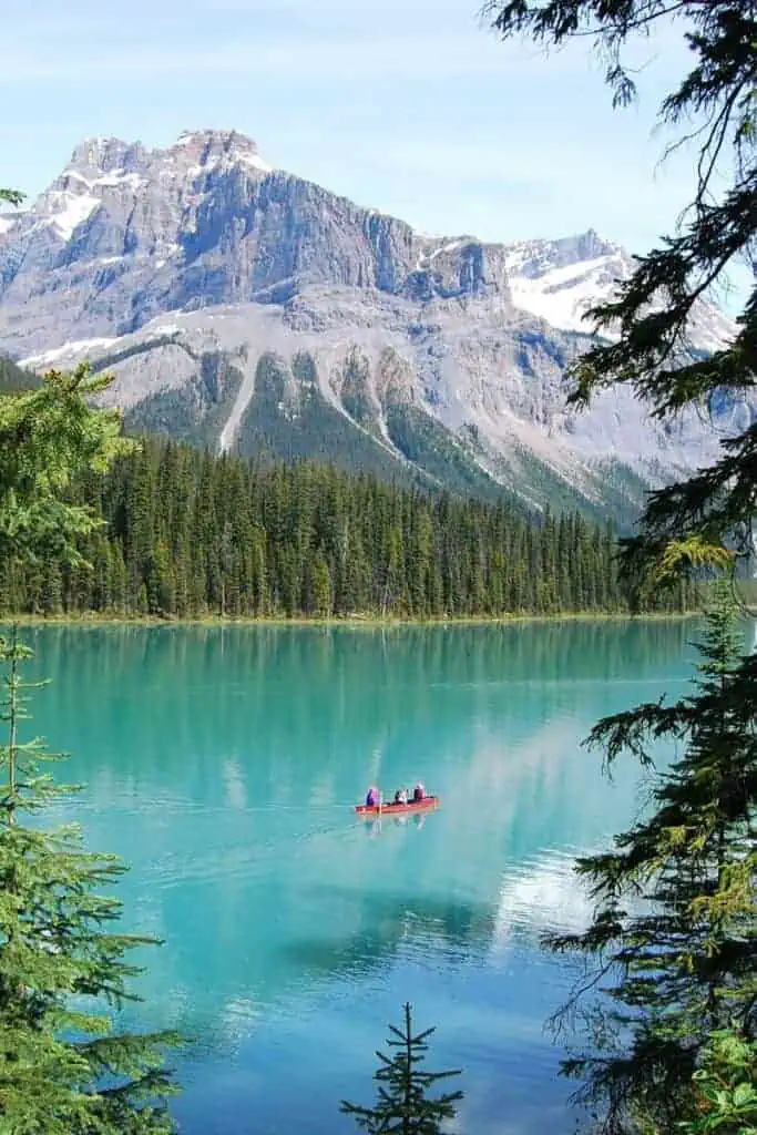 emerald lake in banff, alberta, canada with a red canoe gliding on turquoise water, surrounded by dense pine forests and towering rocky mountains dusted with snow