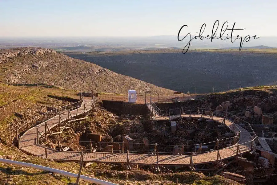 göbeklitepe, the world's oldest known temple complex, with circular stone structures and wooden walkways set against a vast, rolling landscape in turkey