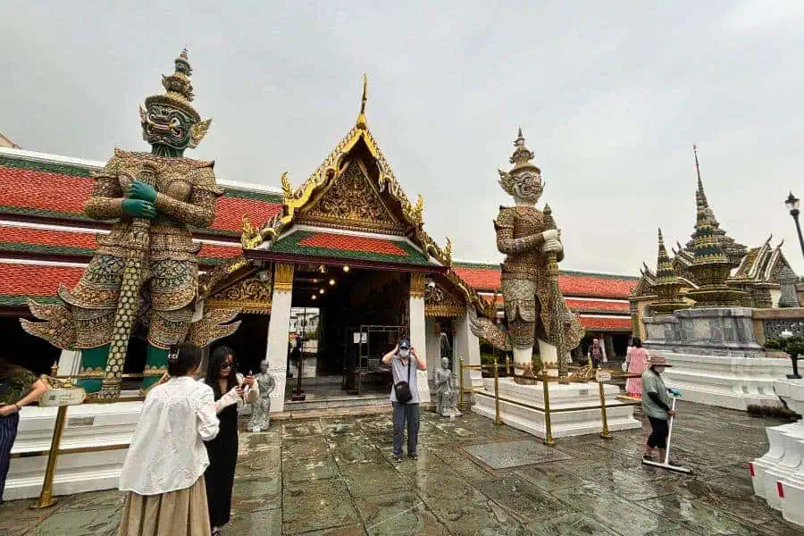 visitors taking photos near the towering guardian statues at wat phra kaew at grand palace in bangkok