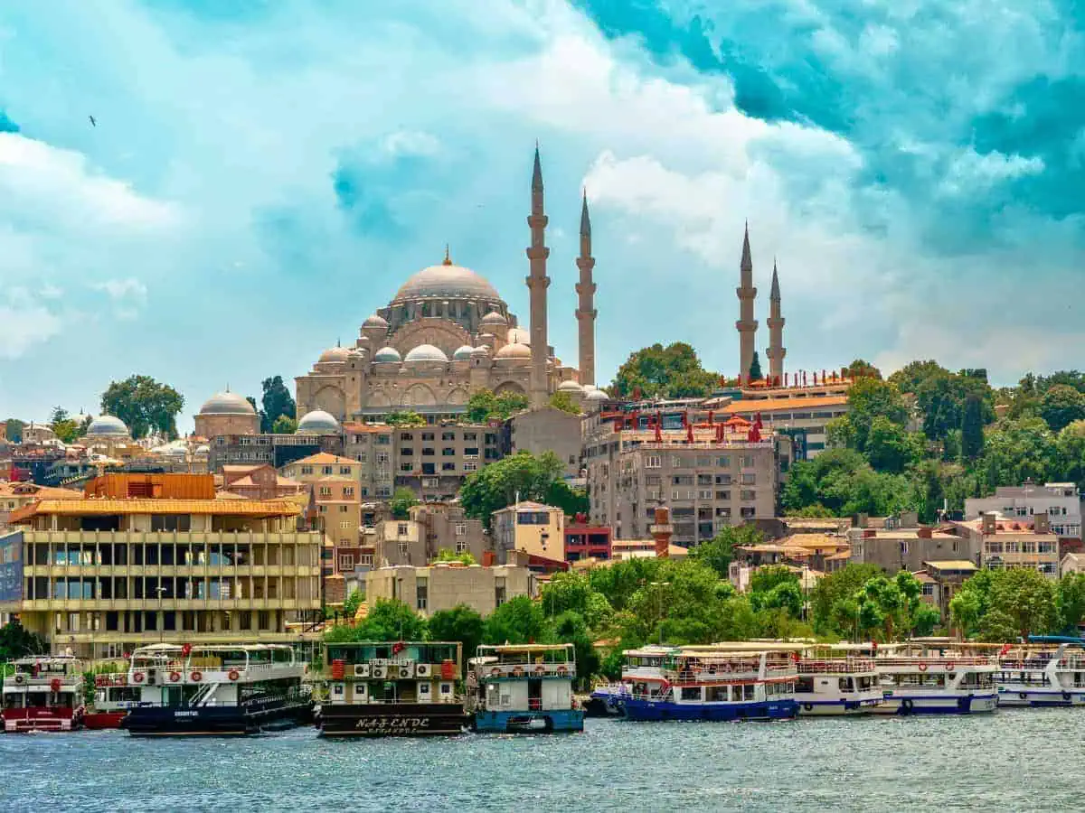 historic mosque with towering minarets overlooking the waterfront in istanbul, turkey, with colorful boats docked along the shore and a bright blue sky above