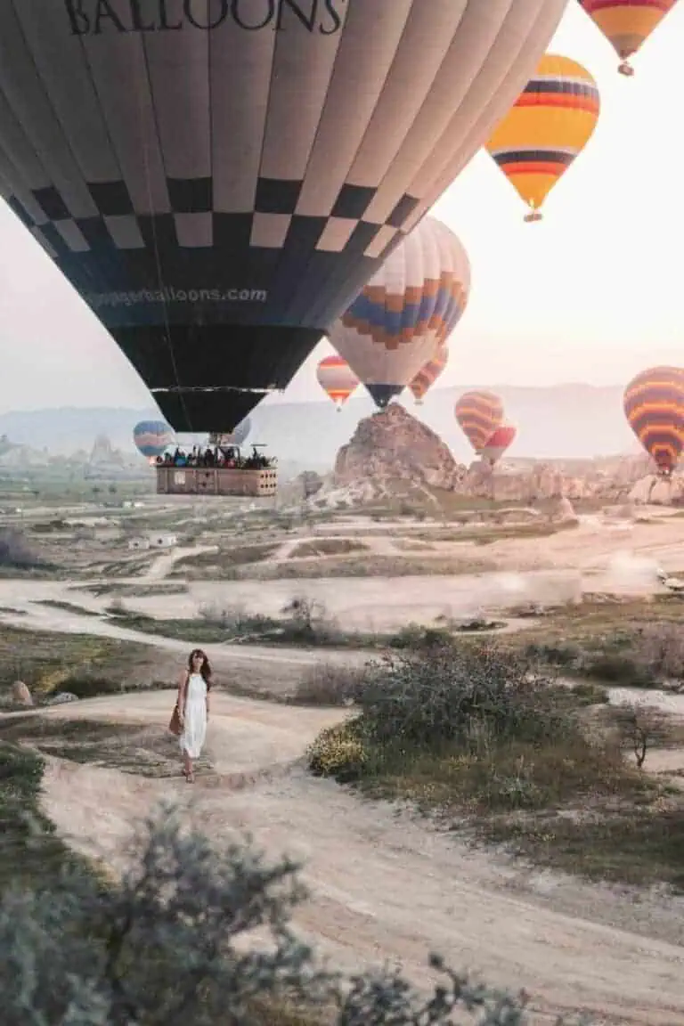 colorful hot air balloons floating over rocky landscape at sunrise in cappadocia, turkey with a woman walking below