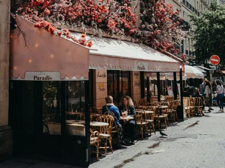 A charming Parisian café called Le Paradis with cascading pink and red flowers covering the building facade, outdoor seating on a cobblestone street, Paris, France