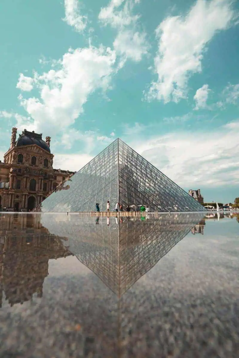glass pyramid of the louvre museum reflecting in water under a bright sky in paris, france