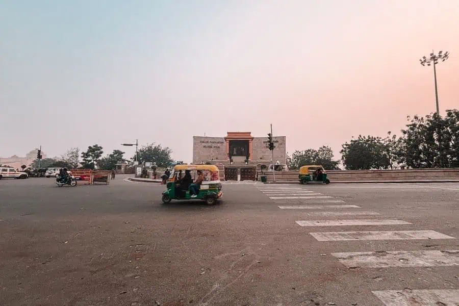 lucknow street scene with auto rickshaws crossing a wide road near a heritage building at dusk