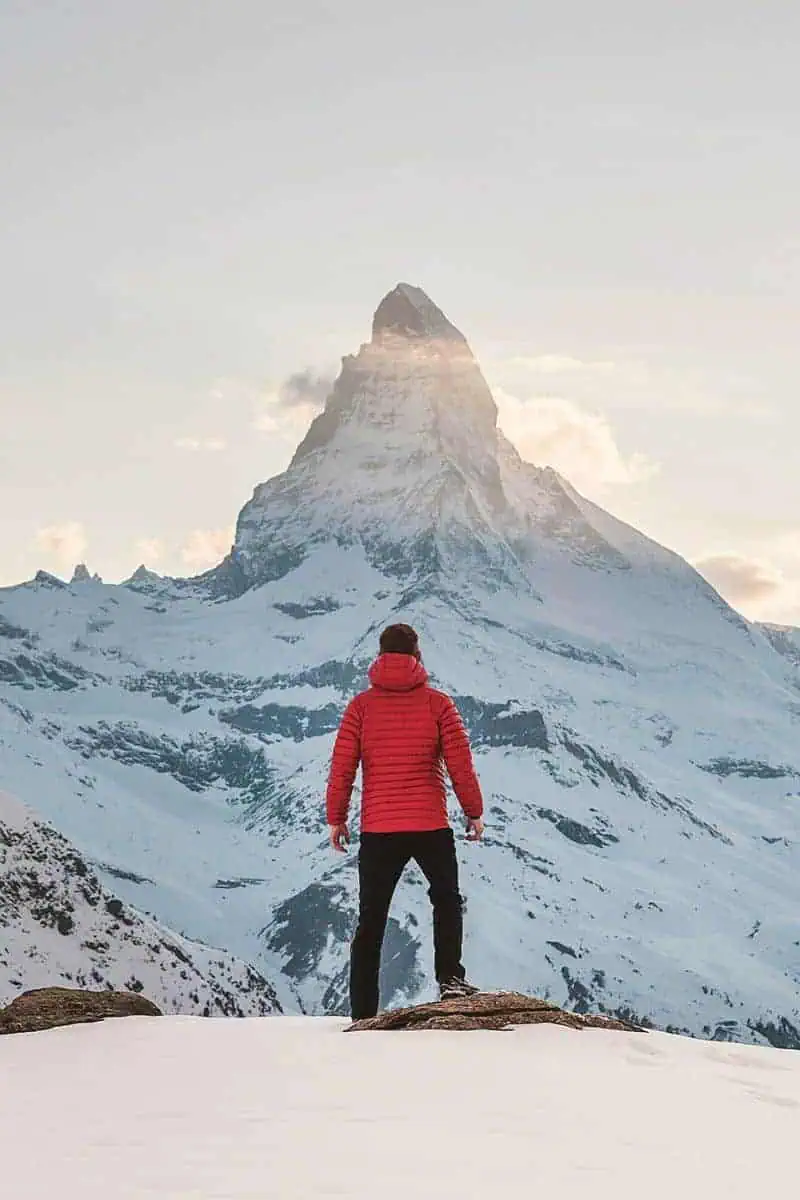 man in red jacket standing in front of iconic matterhorn mountain in zermatt switzerland