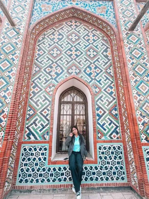 my teen girl posing by a colourful tiled wall at khudayar khan palace in kokand