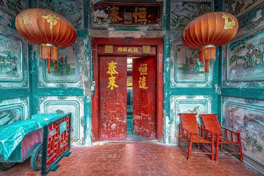 old entrance with rustic red door and blue walls and hanging chinese lanterns of so heng tai mansion in talat noi neighborhood of chinatown in bangkok