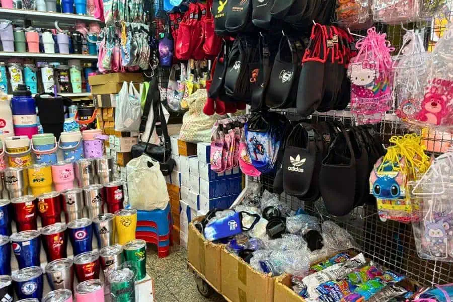a shop at sampheng market in chinatown in bangkok with a variety of items such as water bottles, backpacks, and trinkets at cheap prices 