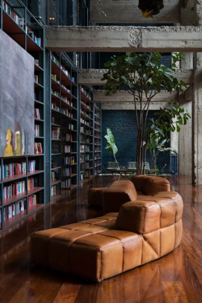 cozy reading lounge with modern brown leather sofa, tall bookshelves, and indoor tree at stamba hotel in tbilisi