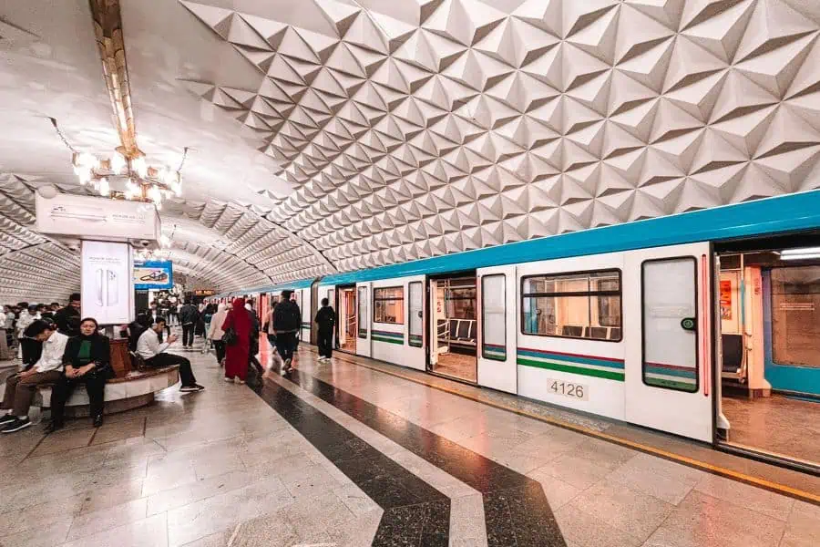 tashkent metro platform with a stopped train, passengers waiting and sitting under a white geometric patterned ceiling