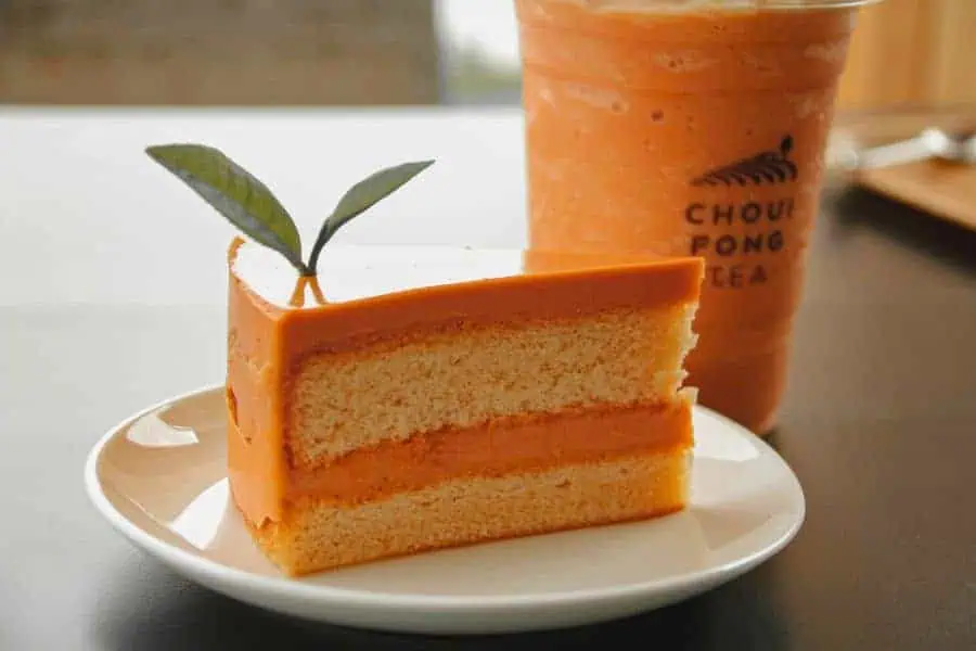a slice of thai tea fudge cake, topped with a decorative leaf, served on a white plate beside a glass of iced thai tea at choui fong tea plantation cafe in chiang rai, thailand