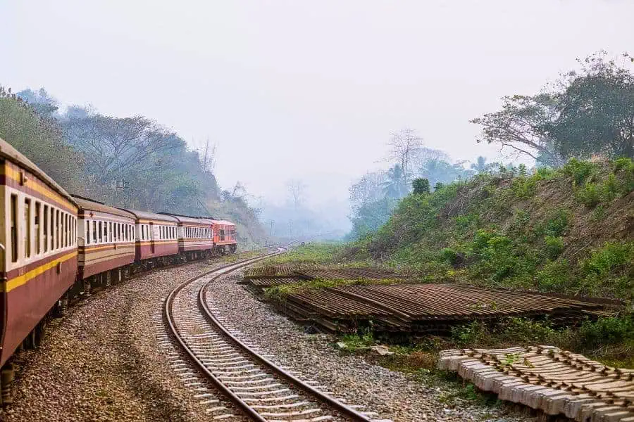 train traveling through lush countryside on a curved railway track, surrounded by greenery and misty hills
