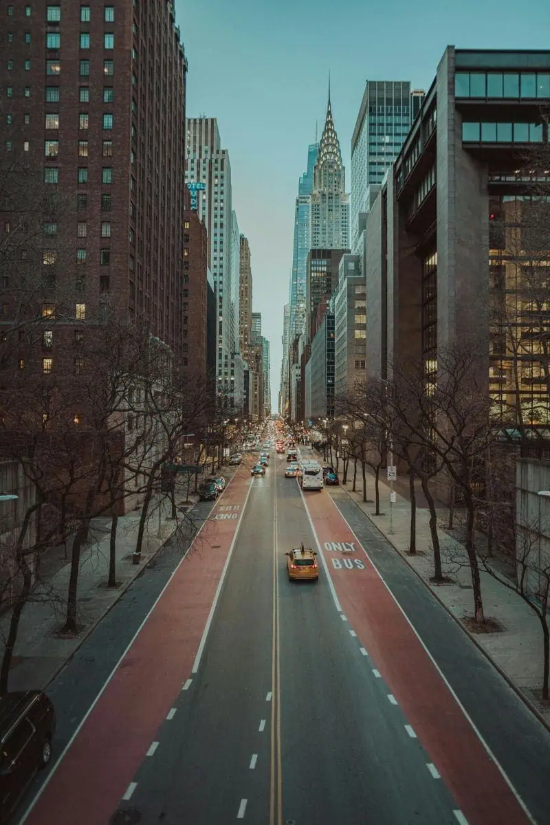 a busy street in new york city lined with tall skyscrapers, with yellow taxis and cars driving toward the horizon, and the chrysler building rising in the background under a clear blue sky