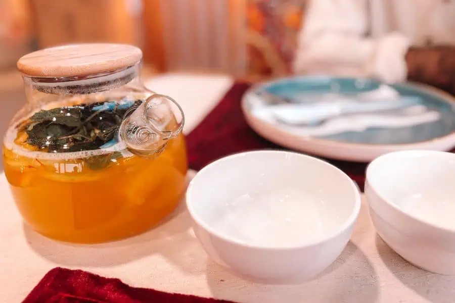 glass teapot of uzbek green tea with herbs served alongside small white bowls on a dining table