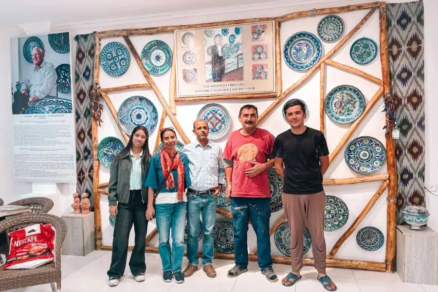 our family posing with uzbek potters at sharofiddin yusupov’s ceramics workshop in rishton, run by his son and grandson, surrounded by vibrant hand-painted blue pottery inside the international ceramics centre