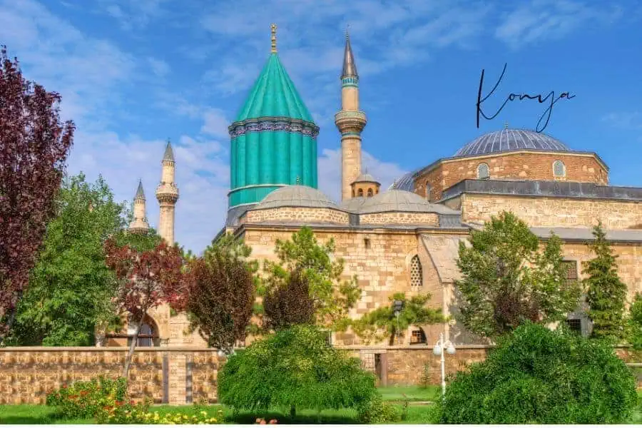 iconic mevlana museum in konya, with its vibrant turquoise dome and minarets surrounded by lush gardens under a bright blue sky