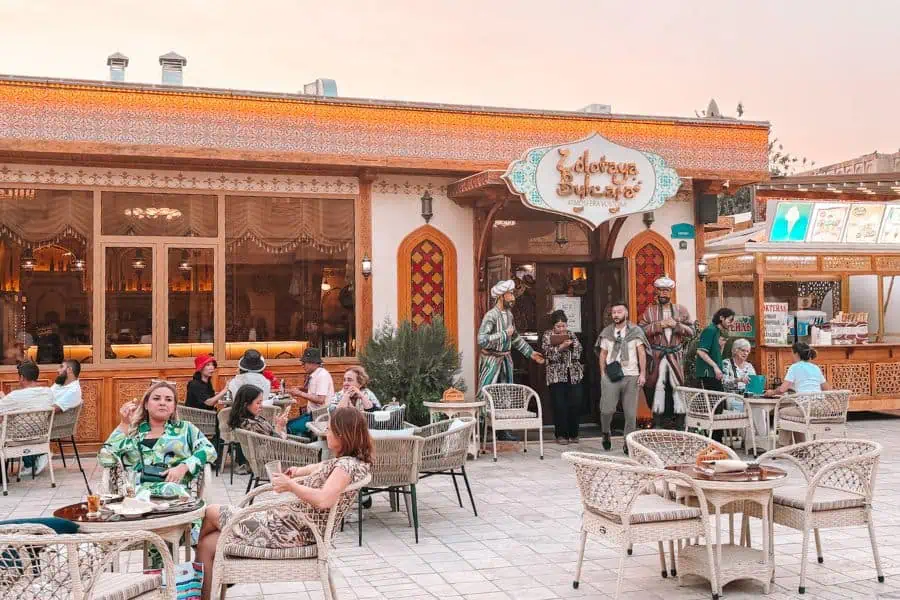 outdoor seating at zolotaya bukhara restaurant with traditional decor, wicker chairs, and diners in the historic old city